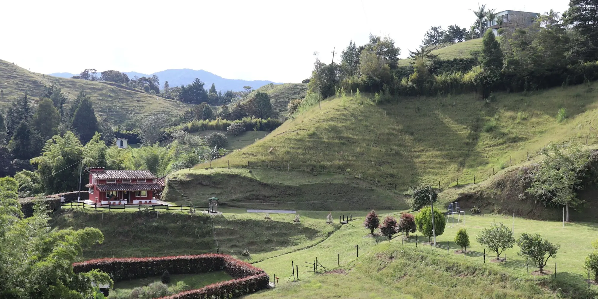 A farmhouse on hillside pasture with forest edges and fenced paddocks in El Retiro, Antioquia, Colombia.